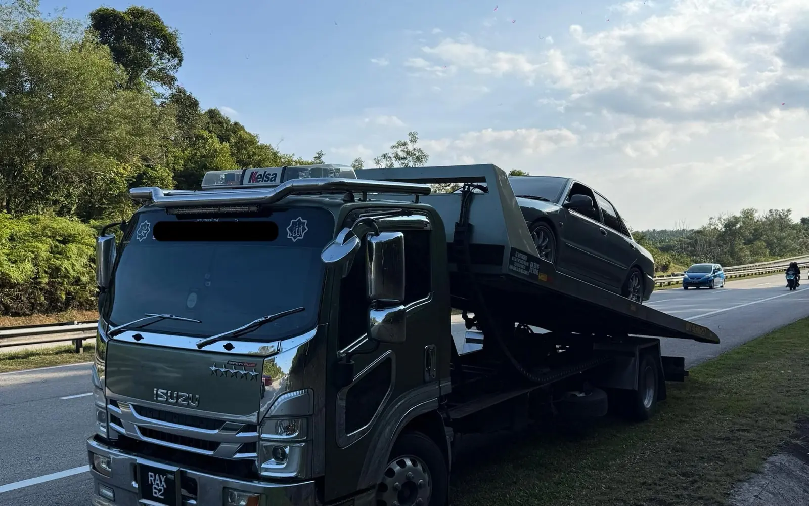 Trak flatbed memuatkan kereta sedan di bahu lebuhraya